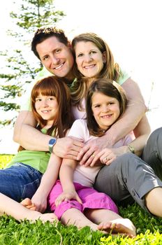 Portrait of happy family of four sitting on grass at the park hugging