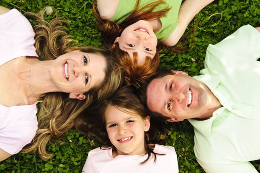 Portrait of happy family laying  on grass looking up heads together