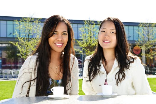 Two girl friends sitting and having drinks at outdoor mall