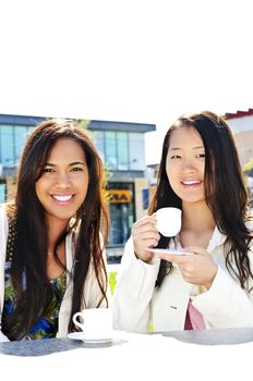 Two girl friends sitting and having drinks at outdoor mall