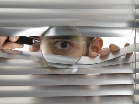 A man is peeping through the blinds with a magnifying glass.