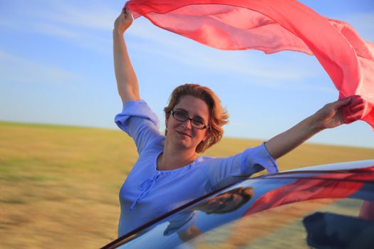 Woman with a pink scarf leaning out of a moving automobile.
