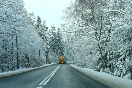 Yellow truck passing the road in snowy forest