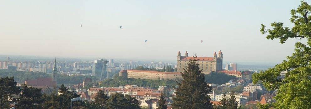 panorama photo of bratislava city, castle in distance, photo taken from slavin, hot air balloons in thy sky