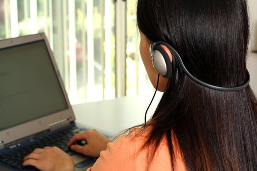 A woman working on a laptop and listening to music using headphone in an office
