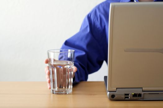 A businessman working on a laptop and holding a glass of water