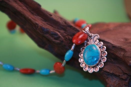 Colorful red and blue turquoise necklace on wooden branch with green background.