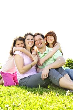 Portrait of happy family of four sitting on grass at the park hugging