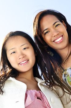 Two diverse young girlfriends smiling into camera