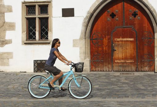 Young woman riding bicycle in front of an old builidng in a city square.