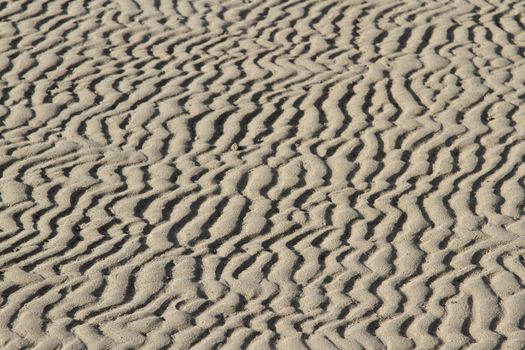 Sand textured with abstract patterns of waves, lines and ruts highlighted by shadows running into the distance.