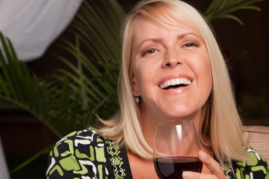 Beautiful Blonde Woman Smiling at an Evening Social Gathering Tasting Wine.