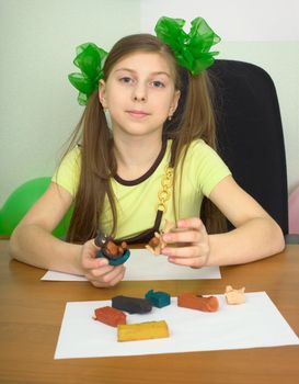 Girl sitting at a table with plasticine in hands