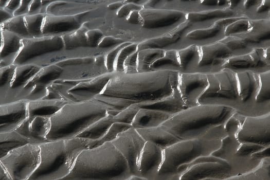 Sand textured with abstract patterns of waves, lines and ruts sourounded by water