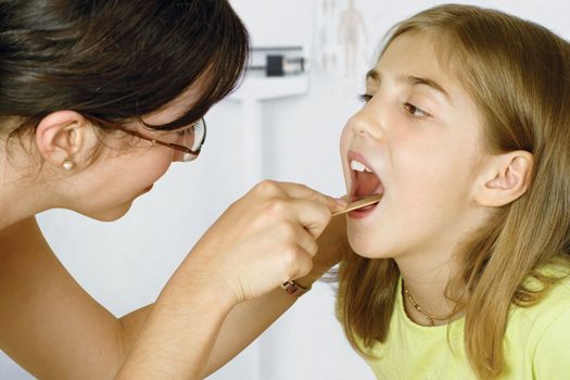 Doctor in her office checking the throat of a young patient.
