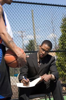 A basketball coach in a business suit sharing a play with a player on the team.  He could be also be a college scout trying to get him to sign a contract.