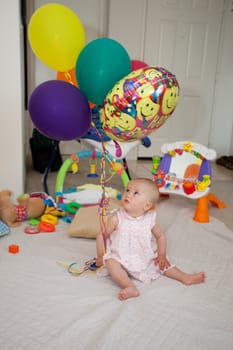 Caucasian baby girl playing with colorful balloons on a floor.