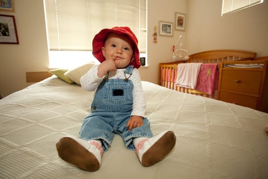 Cute little caucasian baby girl wearing red hat and sitting on a bed.