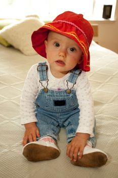 Cute little caucasian baby girl wearing red hat and sitting on a bed.