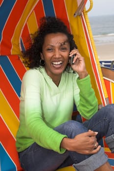 Beautiful woman sitting in a beachchair on a windy day and laughing on the phone
