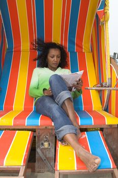 Beautiful black woman sitting in a colorful chair and reading a magazine