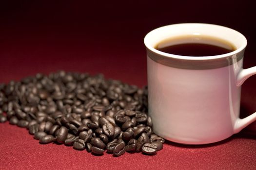 White coffee cup and beans sitting on a red background fade to black