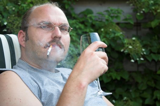 Mature man sitting in his garden chair drinking too much wine and smoking too much