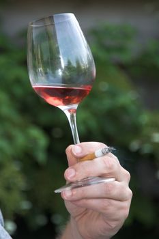 Hand holding a glass and a cigarette outdoors filled with rose