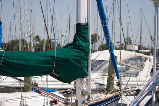Sailboat Masts and Booms captures mast with a green sail cover as well as several poles lines and other nautical types of equipment and rigging in this marine background.
