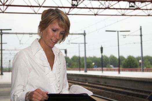 Pretty blond businesswoman working at the trainstation while waiting for the train