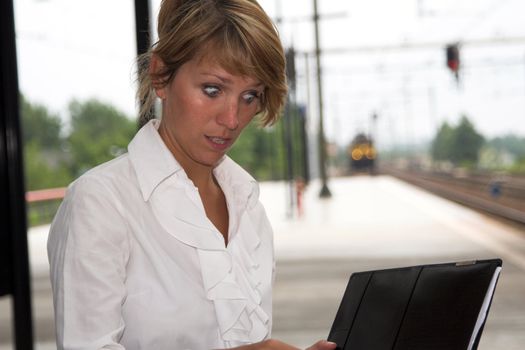 Pretty businesswoman sitting at the trainstation looking shocked at her notes (train is coming in the background)