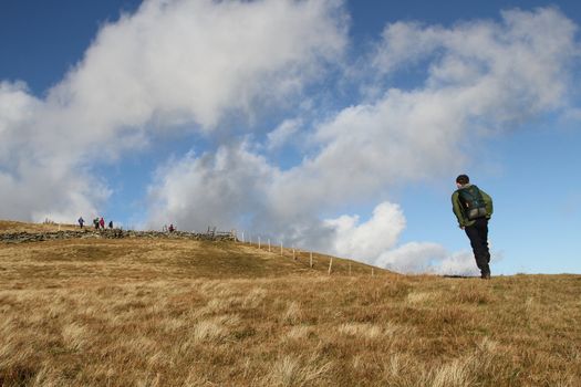 Hill walkers enjoying the great outdoors on a grassy mountainside  with blue sky and cloud.