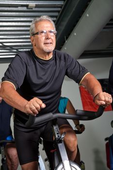 Handsome senior man on spinning bike in the gym