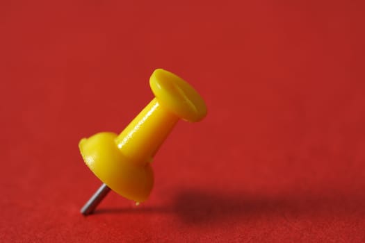 Macro of yellow pushpin against red background