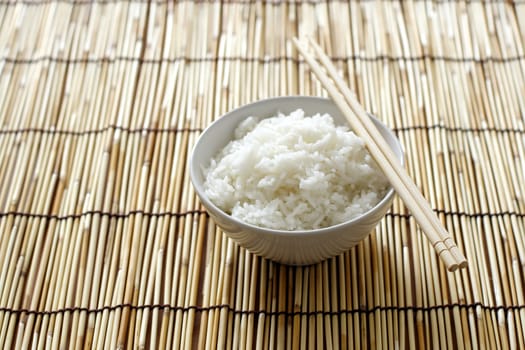 A bowl of rice and chopsticks on bamboo