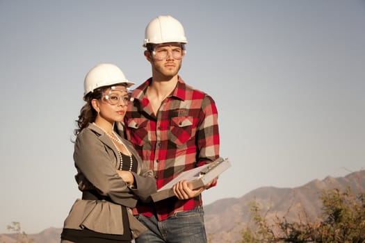 Handsome man and pretty woman outdoors wearing protective hardhats