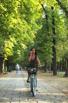 Image of a woman on the phone riding a bicyclein an autumn park