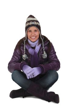 Happy young woman in winter clothes sitting crosslegged against a white background.