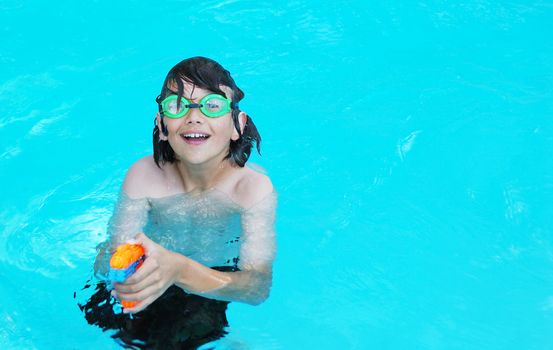 Smiling teenage boy in the pool pointing an orange water gun.