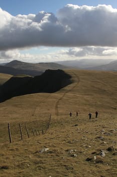 Hill walkers enjoying the great outdoors on a grassy mountainside  with blue sky and cloud.