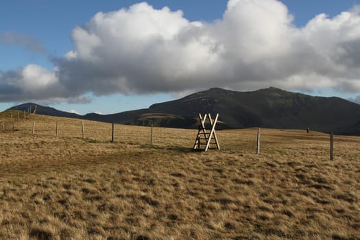 Fence, style and walker on green grass on a mountain with blue sky and clouds.