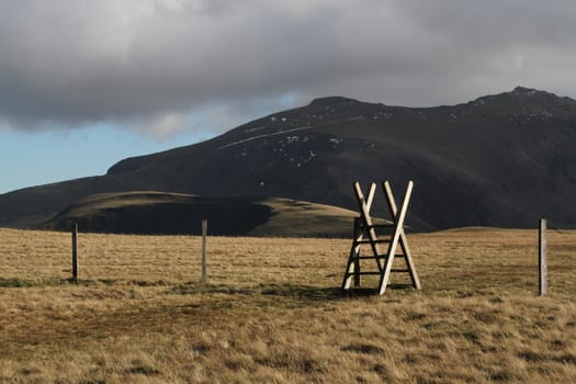 Wooden style over a fence on green grass on a mountain.