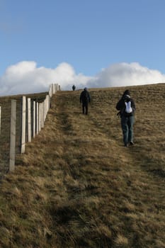 Hill walkers enjoying the great outdoors on a grassy mountainside  with blue sky and cloud.