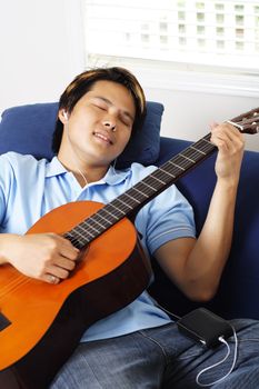 Young man relaxing at home by playing guitar