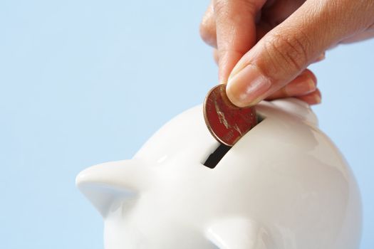 A woman saving a coin into a piggy bank