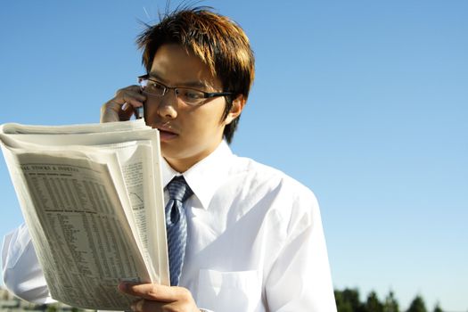 Businessman reading financial newspaper while making a phone call