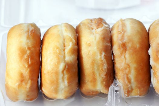 Open plastic container of sticky sugar glazed donuts or doughnuts.