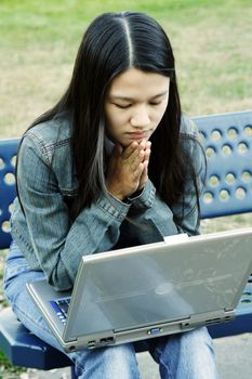 A girl sitting on a bench working on her laptop