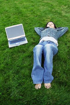 A girl with a laptop taking a nap outdoor in a park