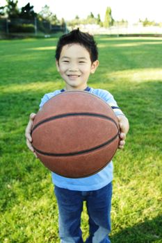 A happy boy handing a basketball (shallow DOF, focus on the ball)